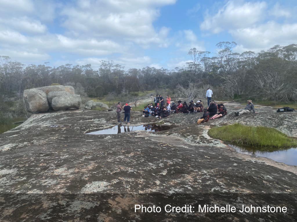 A group of people sitting on a granite outcrop in the bush.